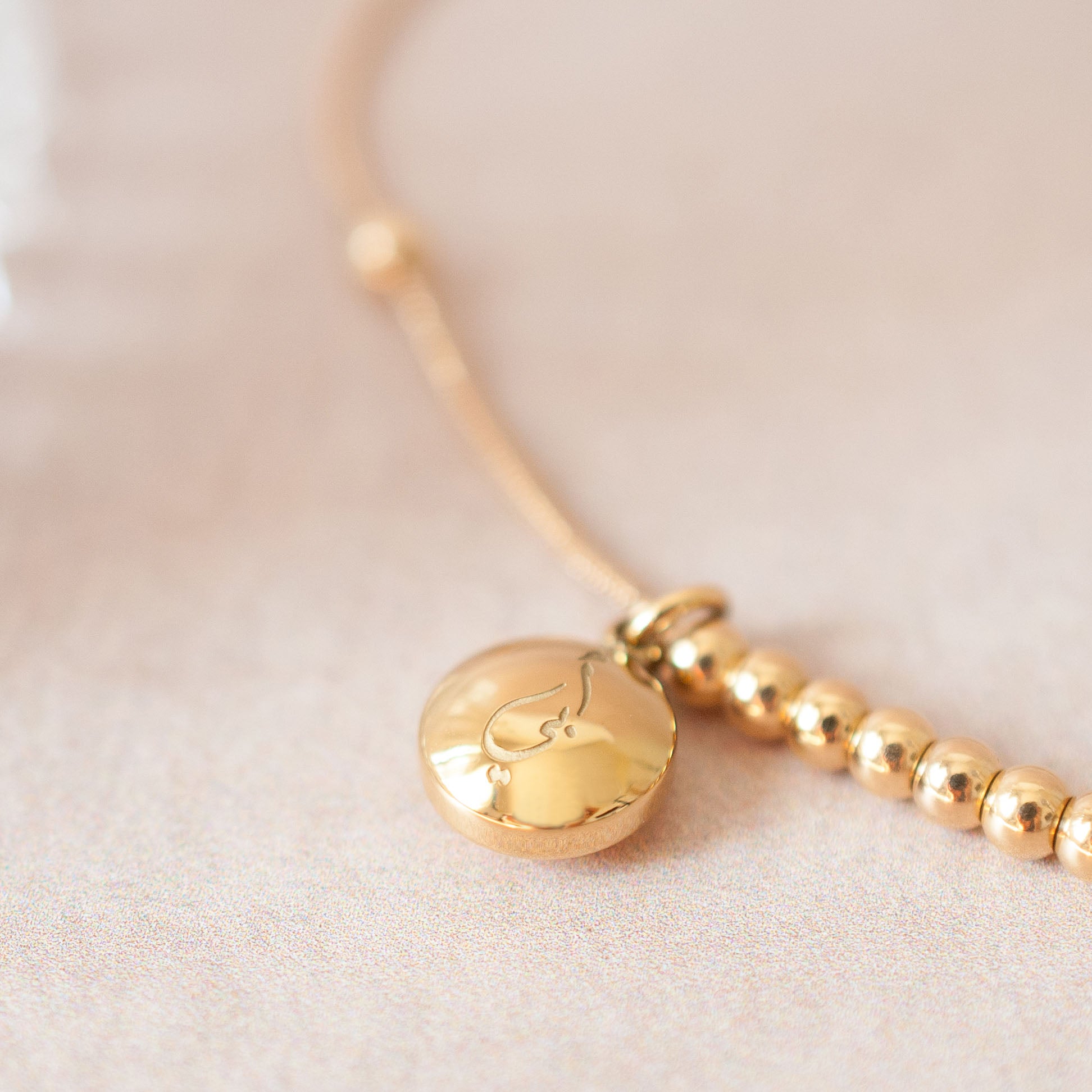 Close up of charm on gold Arabic bracelet showing 'Father' engraved