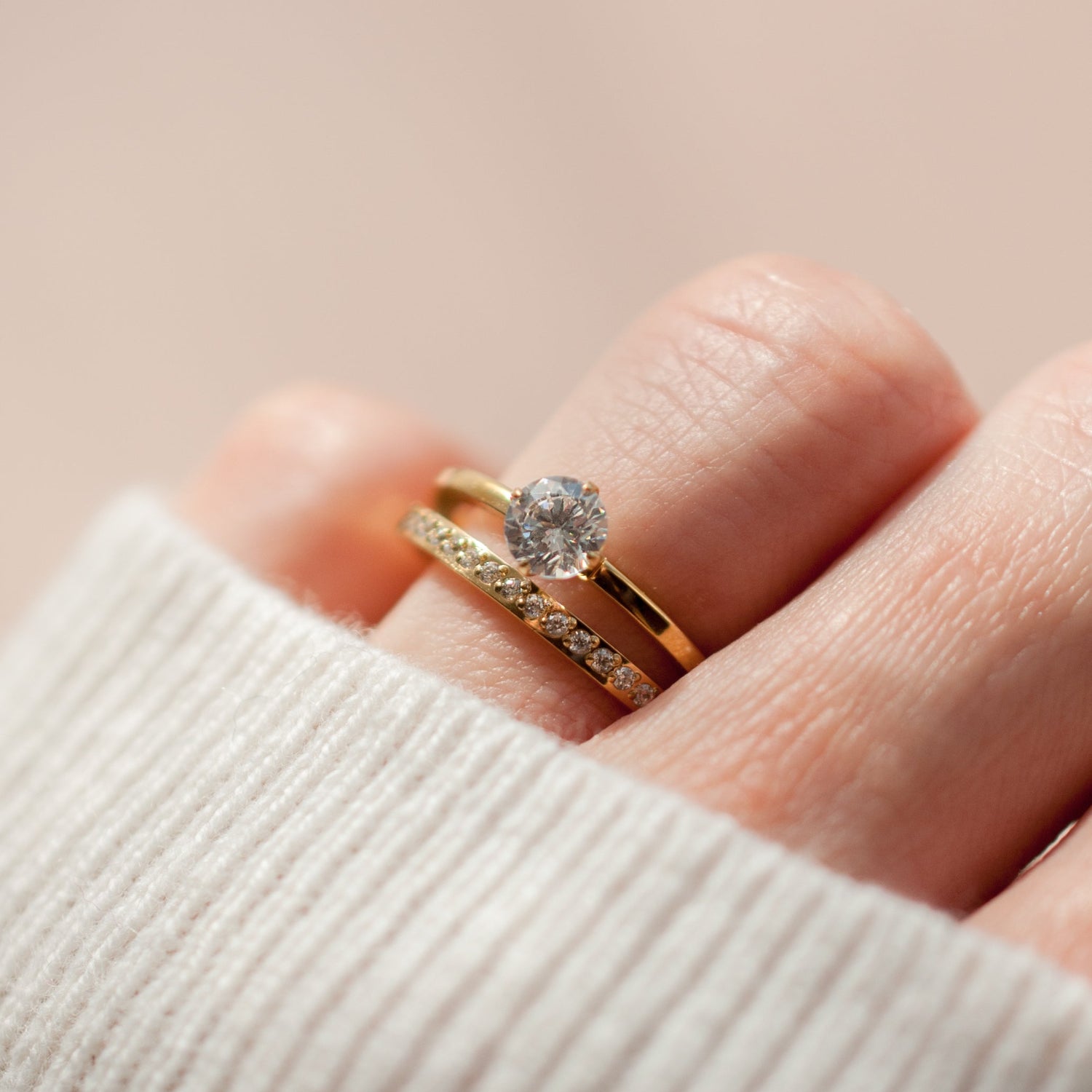 Gold ring with a diamond on a finger against a beige background