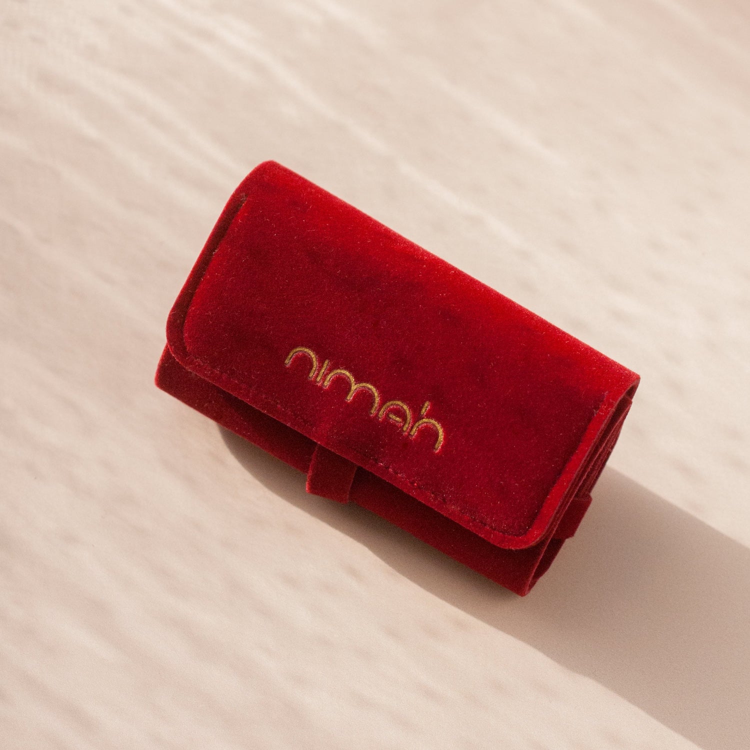 Red velvet pouch with 'nimah' branding on a beige background