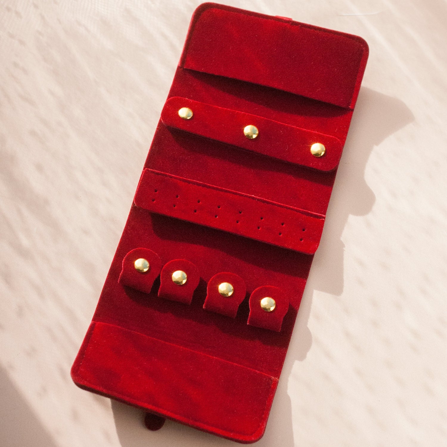 Red velvet jewelry organizer with gold accents on a white textured surface
