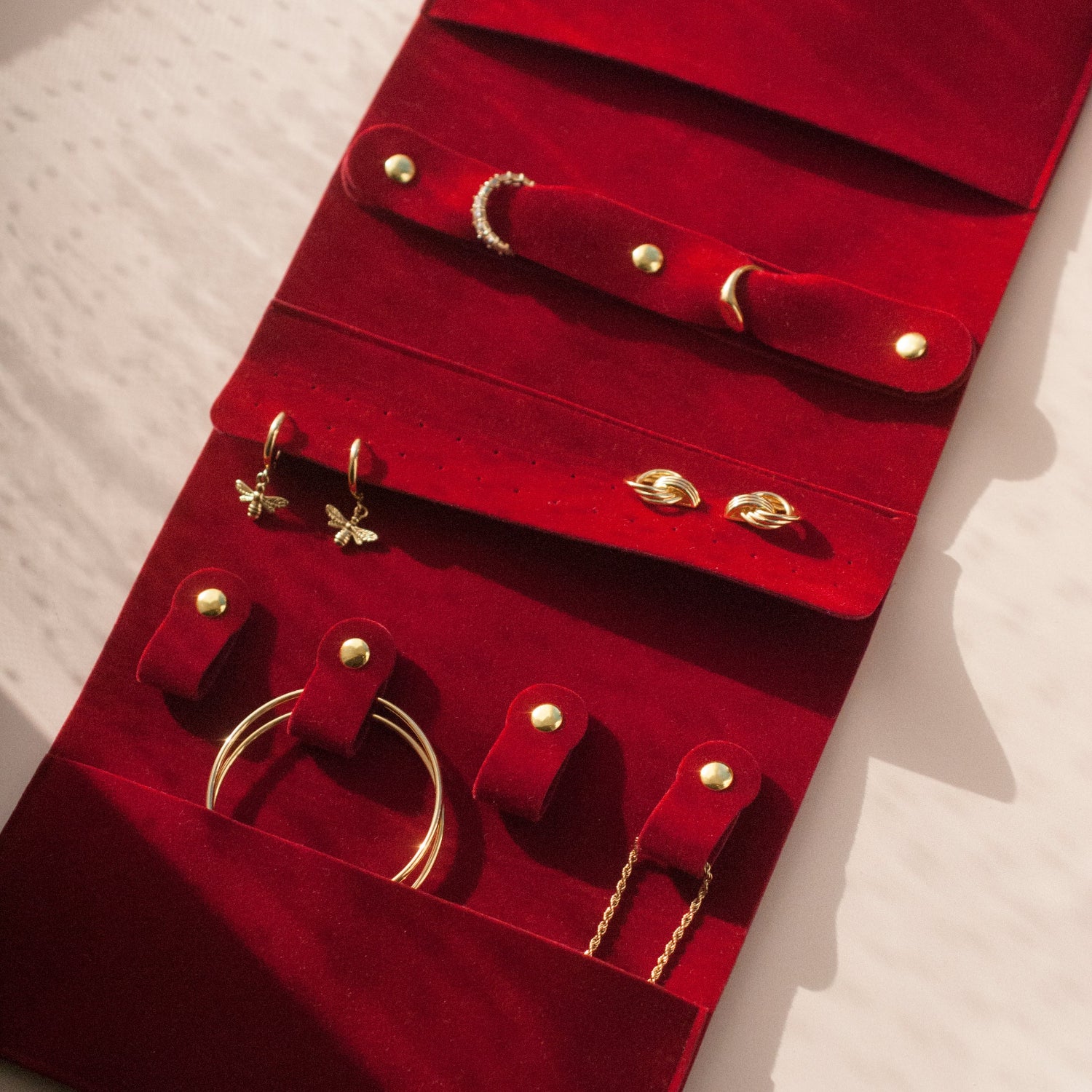 Red velvet jewelry organizer with gold jewelry on a white surface