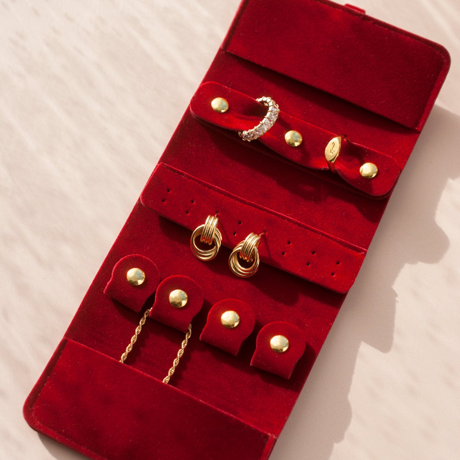 Red velvet jewelry roll with gold jewelry on a light background