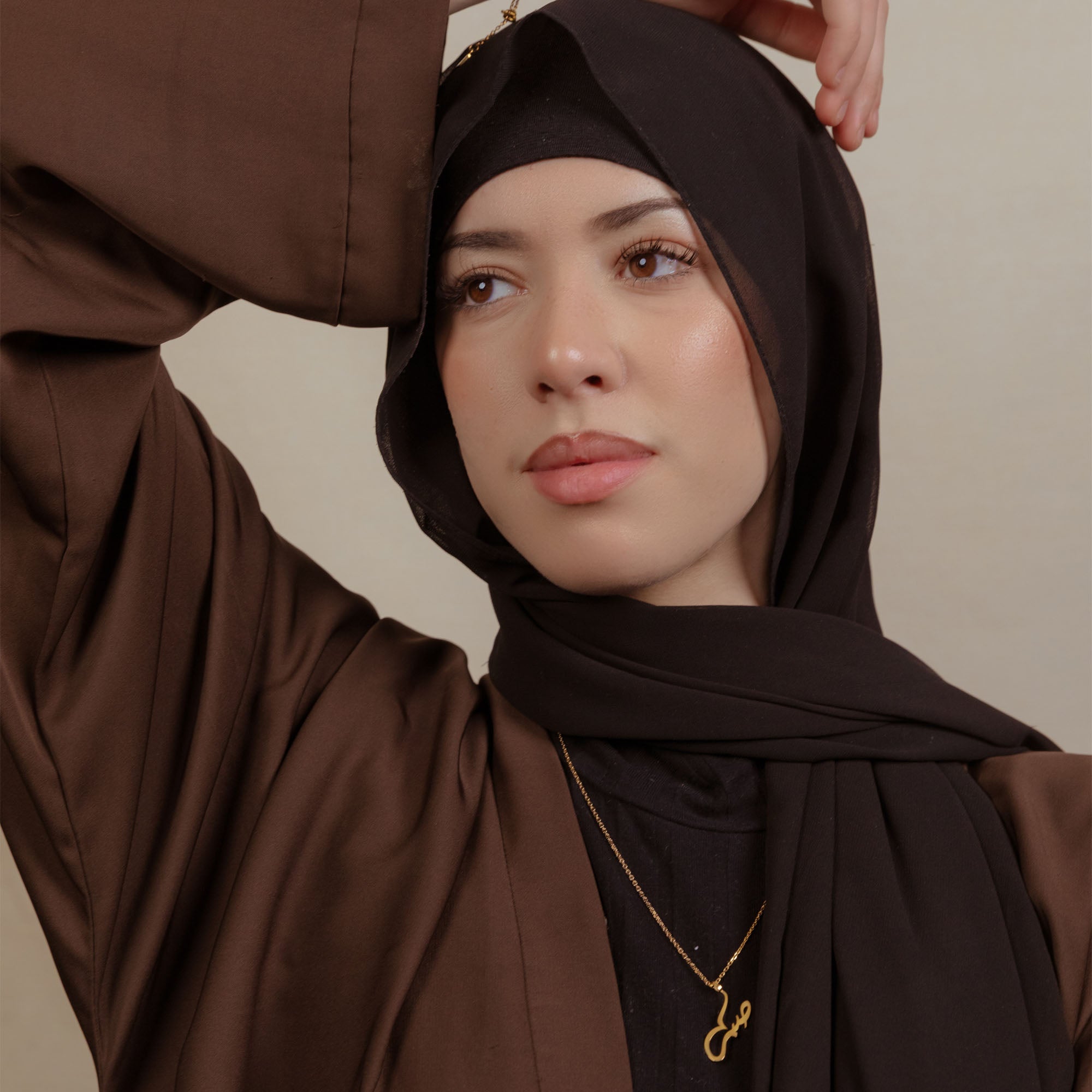 Nimah gold plated necklace worn by woman wearing a black hijab and brown abaya