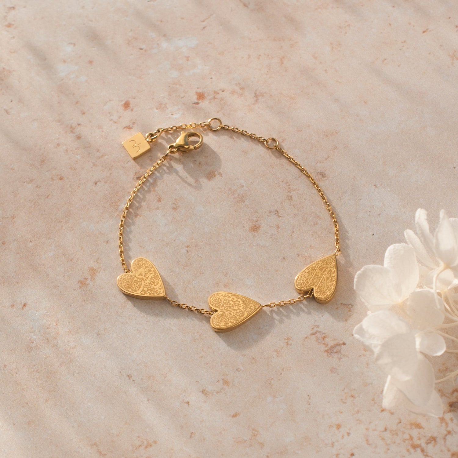 Gold heart-shaped bracelet on a marble surface with a white flower.