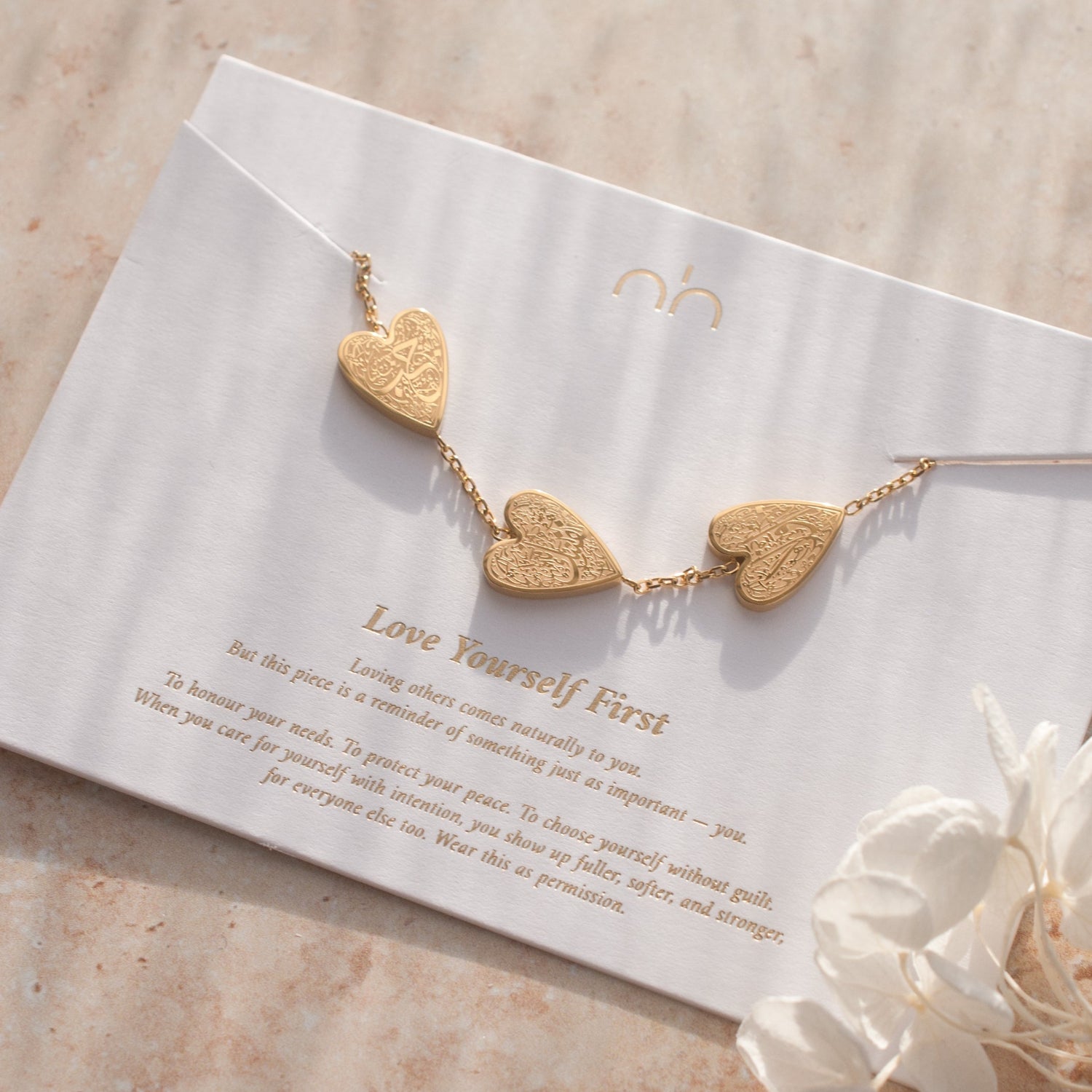 Gold heart-shaped necklace on a card with text, placed on a textured surface with flowers.