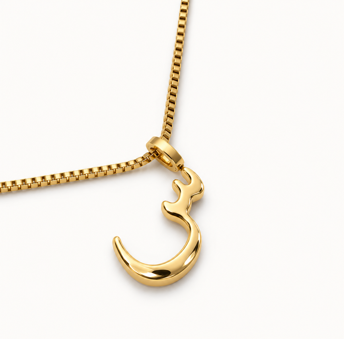 A gold arabic letter pendant necklace featuring a polished Arabic calligraphy character 'seen' on a gold box chain, photographed on a clean white background. brand nimah