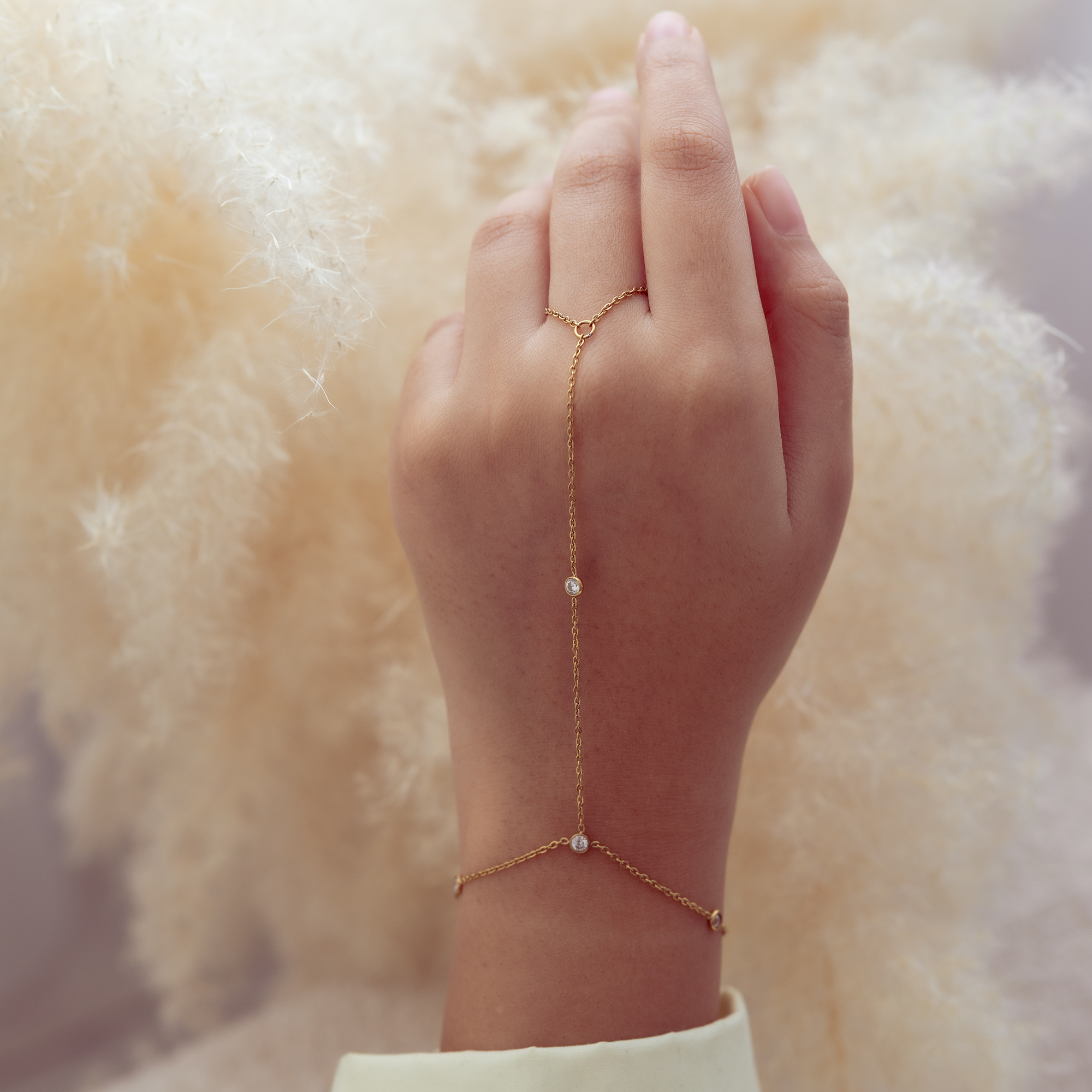 Hand wearing a delicate gold bracelet with small beads against a soft, blurred background